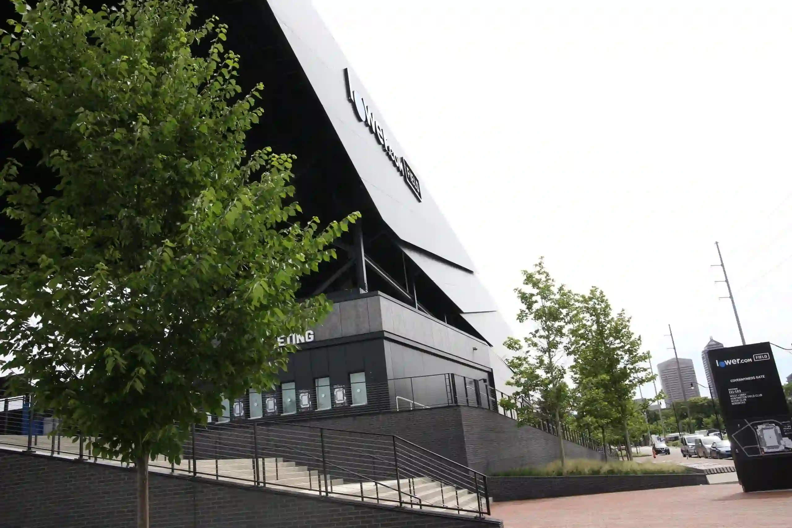 Exterior view of Lower.com Field stadium with its large angled roof canopy, exterior stairs and railings, entrance signage, surrounding trees, and city buildings in the background.