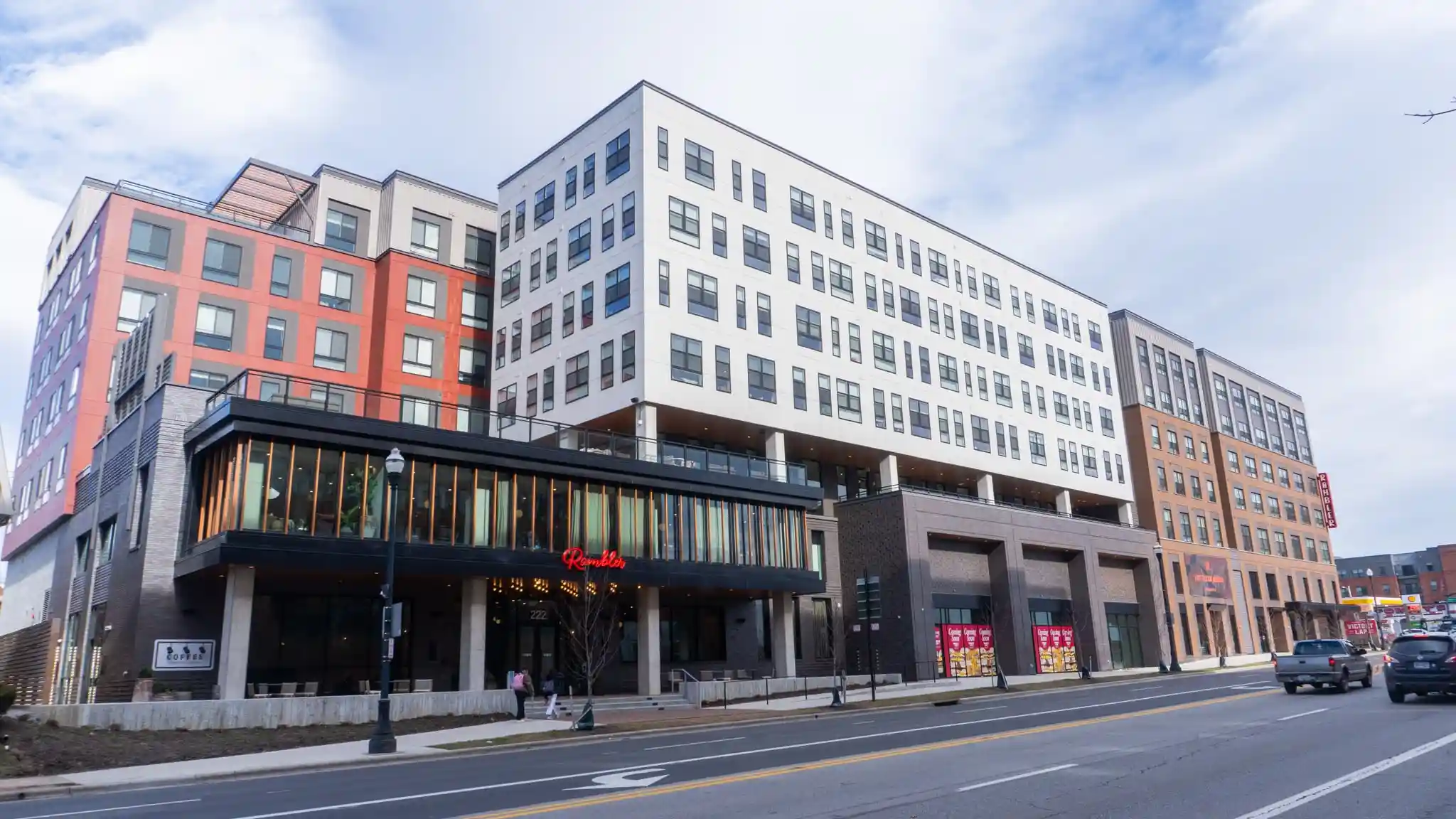 Modern mixed-use apartment building with red, white, and tan brick facades, a glass-walled second level, and a red Rambler sign.