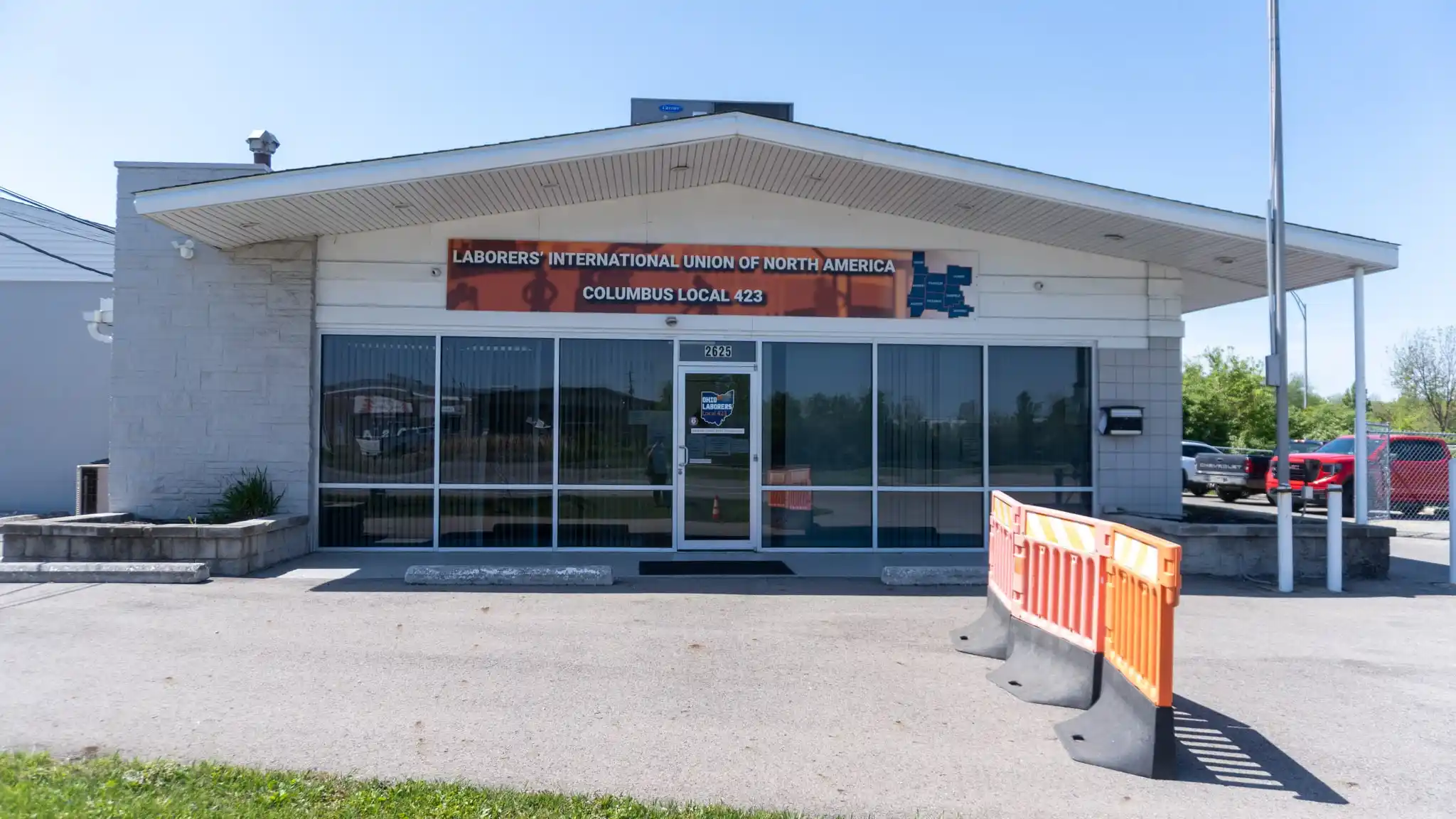 Exterior of the Laborers' International Union of North America, Columbus Local 423 building, a single-story office with large storefront windows and an orange traffic barrier in front of the entrance.