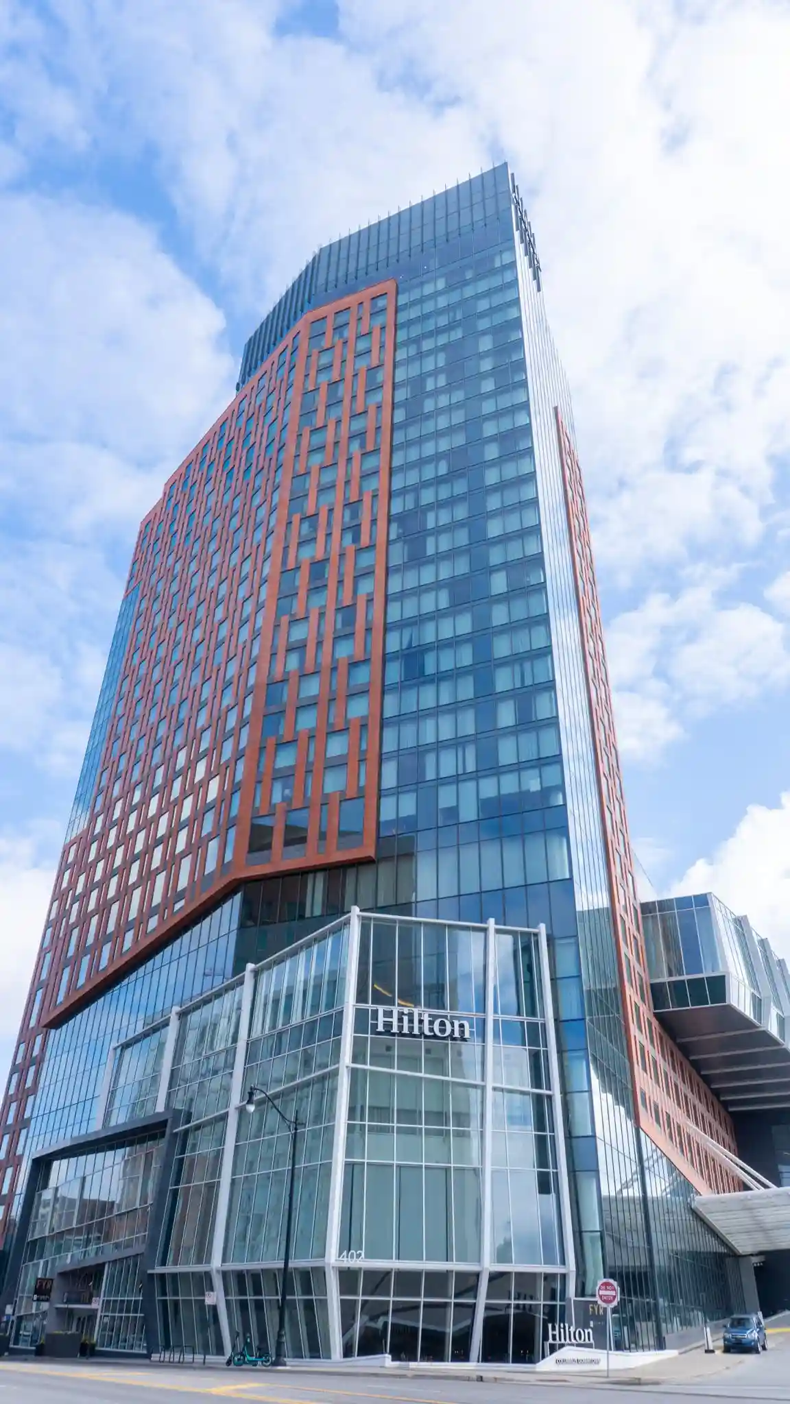 Upward view of the Hilton Columbus Downtown, a modern high-rise hotel with glass and orange-paneled facades against a blue sky.
