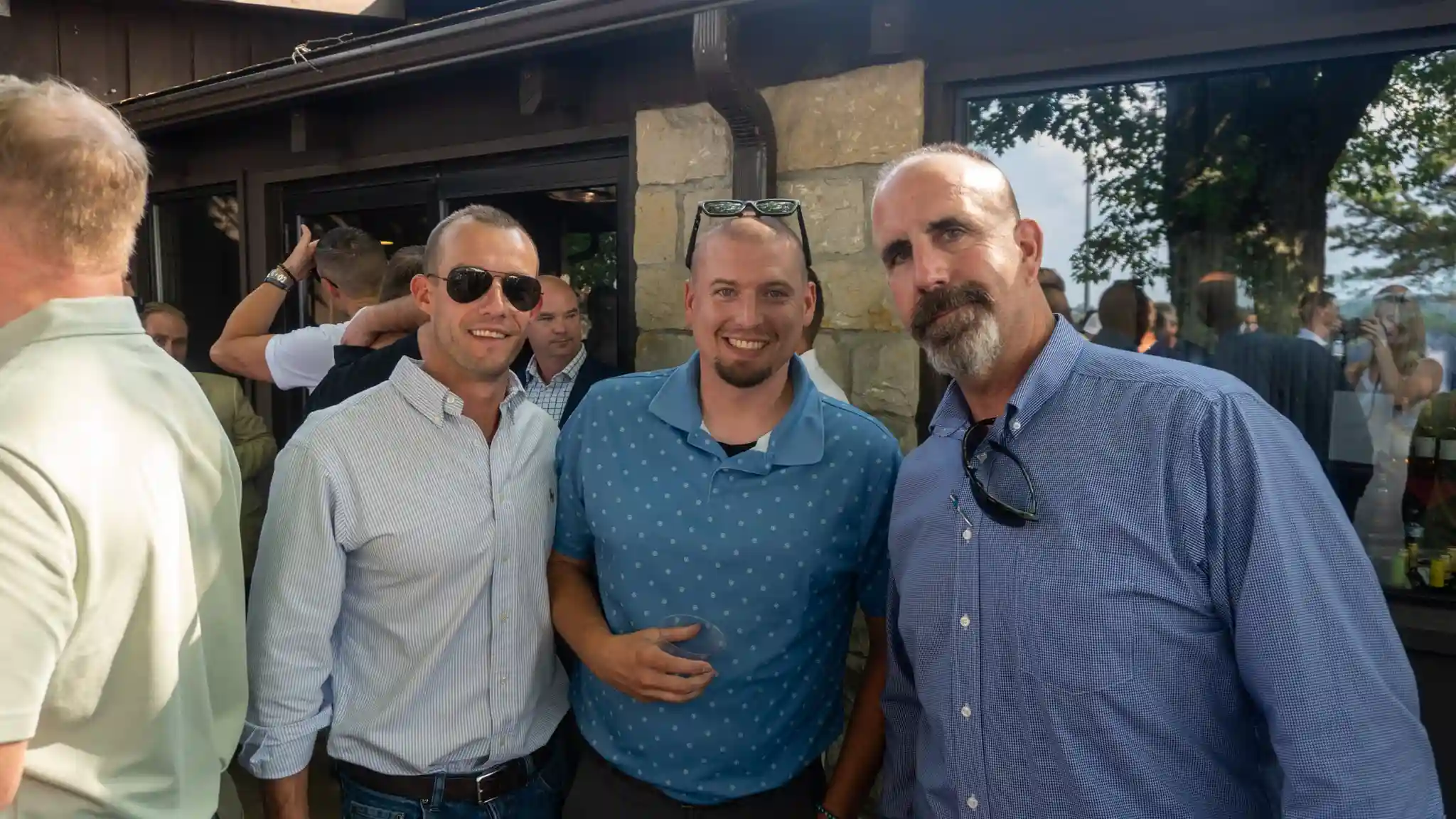 Three men smiling for a photo at an outdoor Kalkreuth gathering