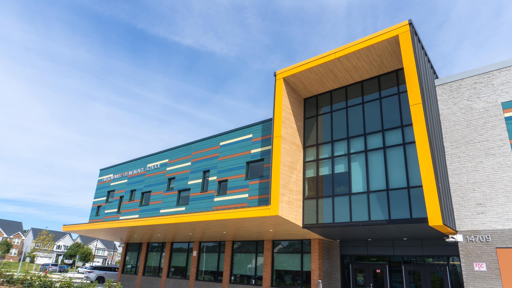 Main entrance of Burtonsville Elementary School, with a glass curtain wall framed in bright yellow trim and black standing seam metal.